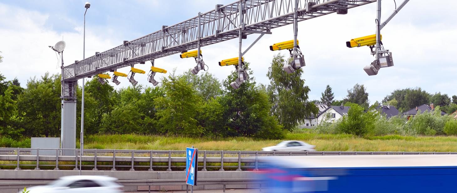 Urządzenie rejestrujące odcinkowy pomiar prędkości zamontowane na bramownicy z kamerami urządzenia skierowanymi na pasy ruchu.